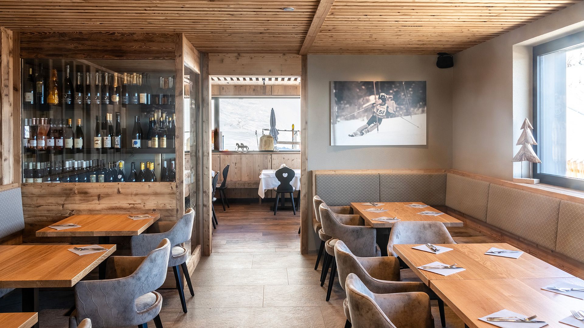 Gemütlicher Innenraum des Alpin Chalet Rosskopf mit warmen Holzwänden, Fenstern mit Blick auf den Schnee und edlen Weinflaschen