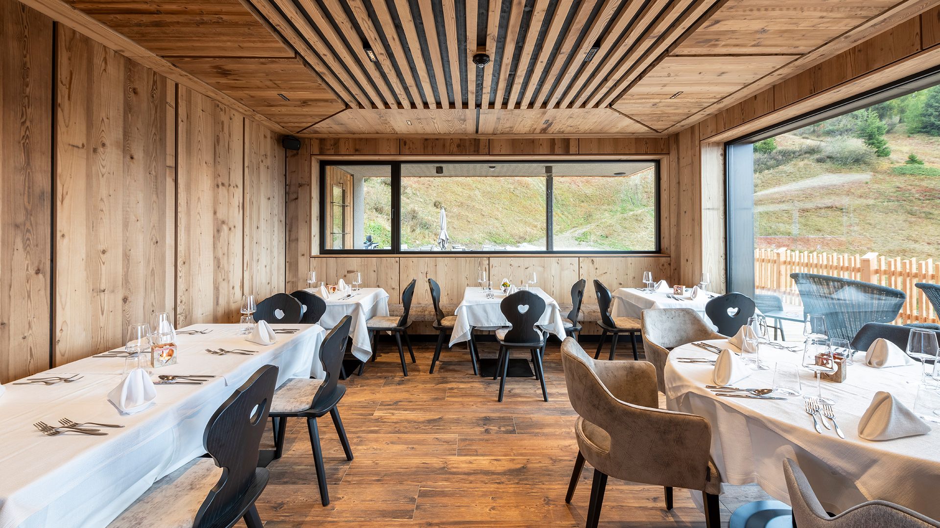 Restaurant aus Holz mit gedeckten Tischen und modernem alpinem Ambiente.	