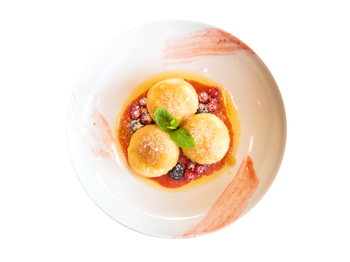 Dessert mit drei süßen Zucker-Knödeln auf roter Beerensauce mit Heidelbeeren, Johannisbeeren und Minzblatt auf einem weißen Gourmet-Teller