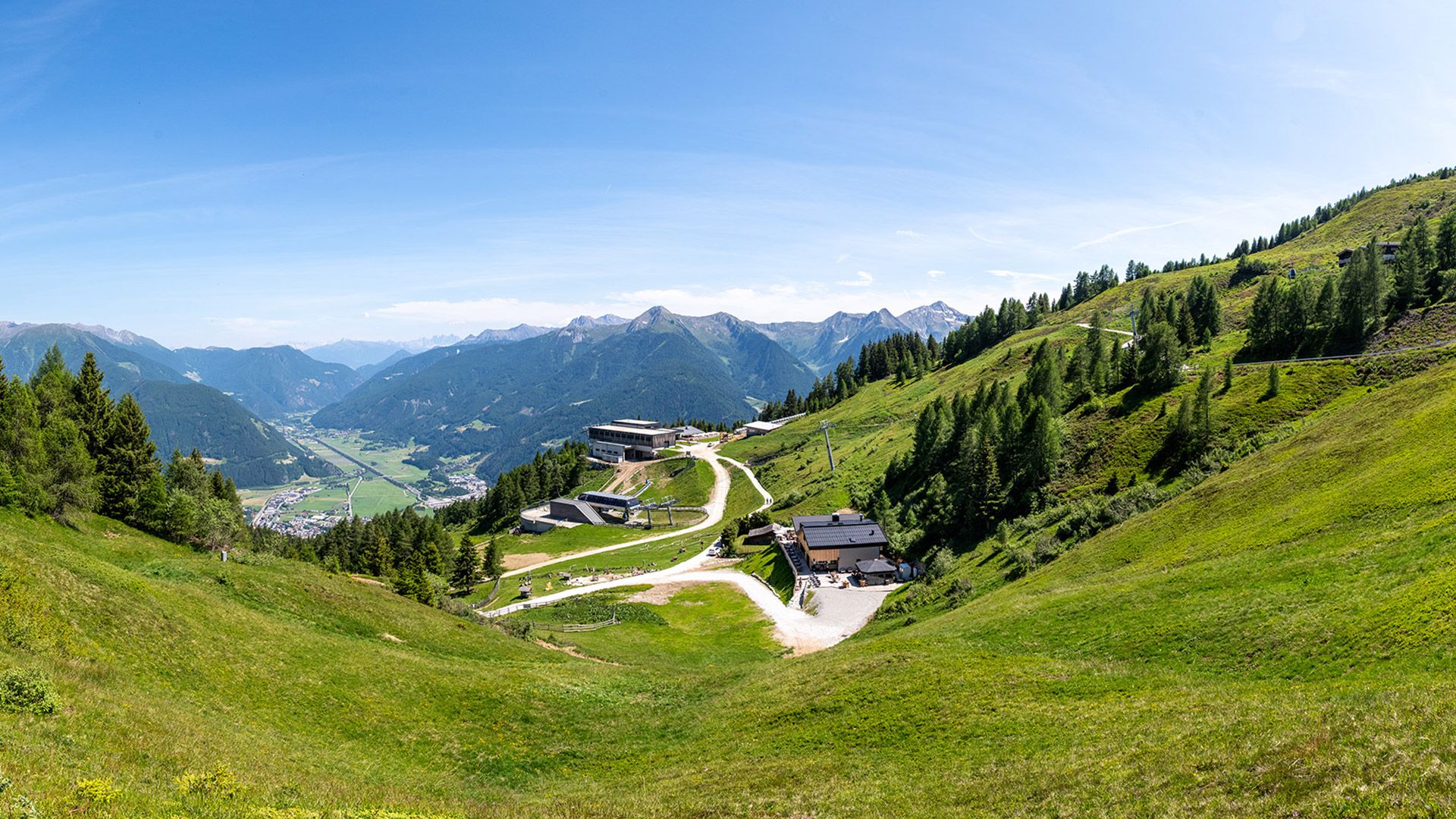 Sommerpanorama mit Bergen, Wanderwegen und alpiner Unterkunft in Höhenlage.